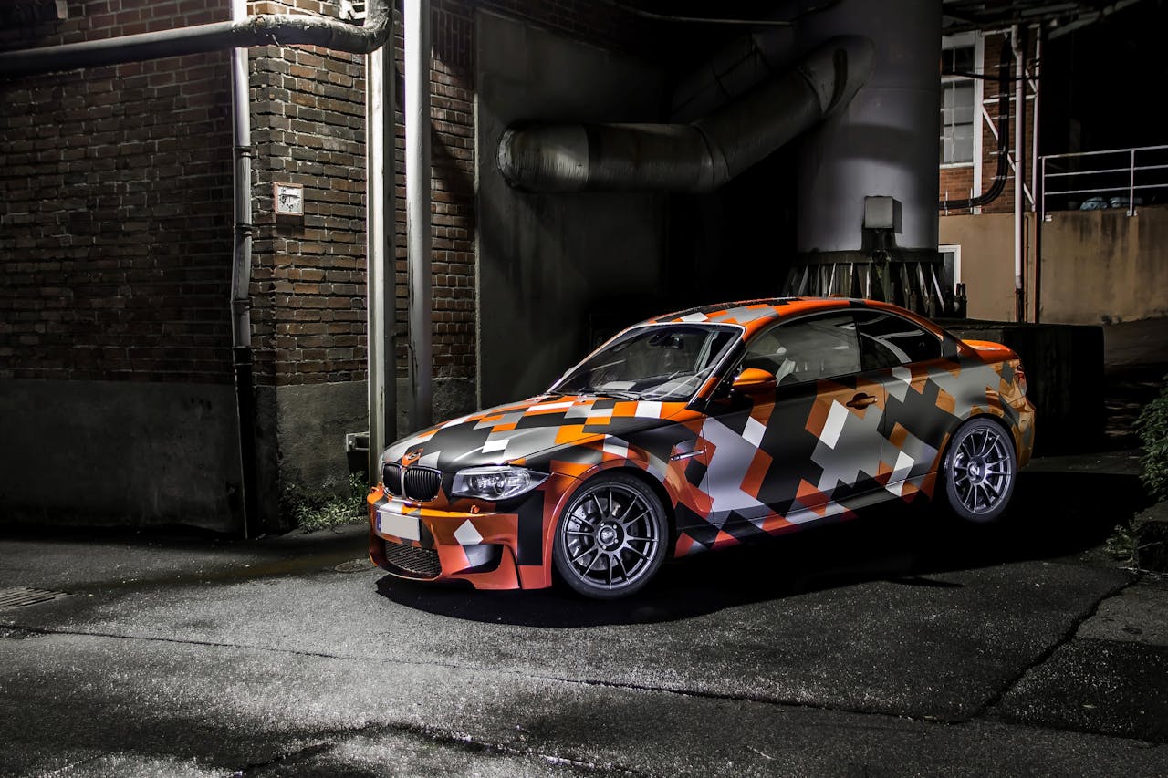 Eye-catching camo-wrapped car parked in an industrial area at night, showcasing vibrant colors and sleek design.