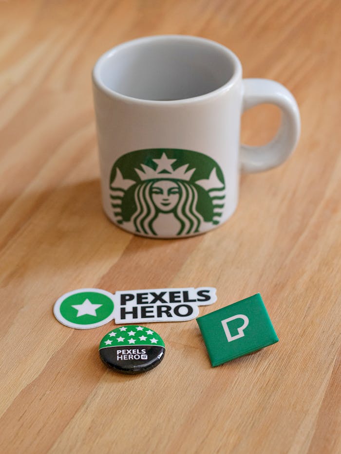 Starbucks mug on wooden table with Pexels Hero stickers, pins, and badge. Perfect for brand-focused content.